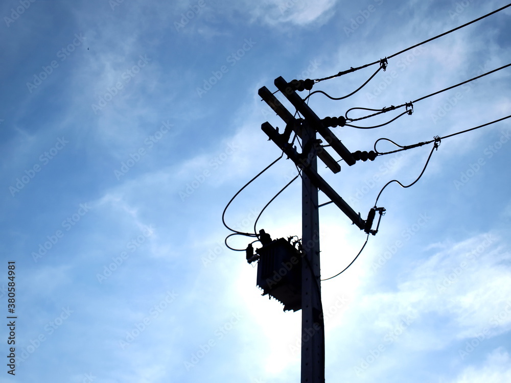 Silhouette of a transformer on a pole. Complete with fuse and an electric cable for converting high voltage AC to low voltage. On the blue sky background there are white clouds. Selective focus Silhouette of a transformer on a pole. Complete with fuse and an electric cable for converting high voltage AC to low voltage. On the blue sky background there are white clouds. Selective focus
