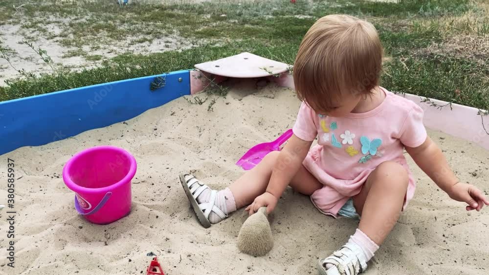 cute caucasian baby girl in pink dress plays in sandbox with shovel and bucket outdoors at summer time in 4k cute caucasian baby girl in pink dress plays in sandbox with shovel and bucket outdoors at summer time in 4k