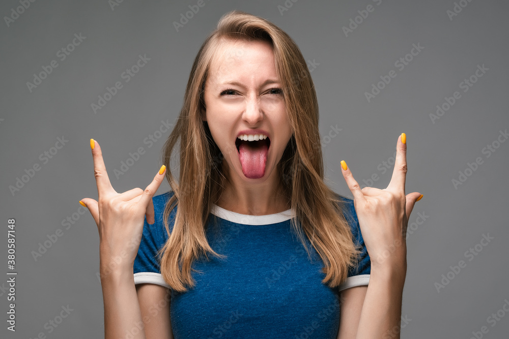 Screaming beautiful blonde girl showing rock sign and looking at camera with open mouth. Studio shot, gray background Screaming beautiful blonde girl showing rock sign and looking at camera with open mouth. Studio shot, gray background
