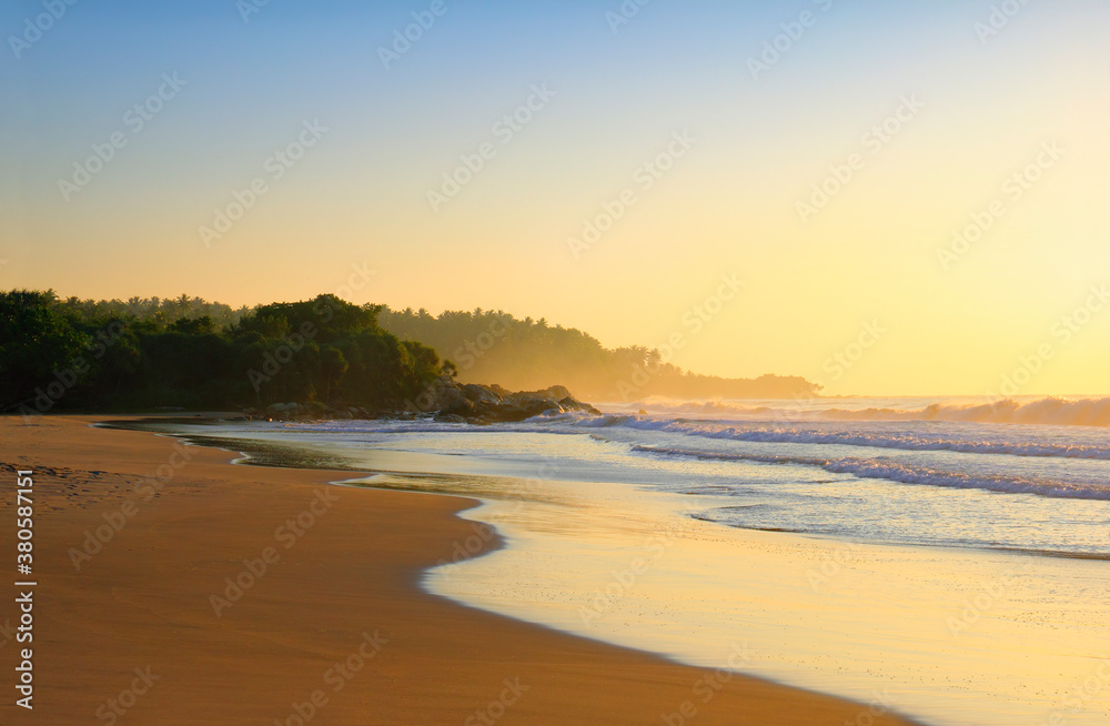 Beautiful scenic view - sea surf, wet sand, rocks and wood against the background of colorful morning sky before the sunrise in Tangalla beach, Sri Lanka island, Indian Ocean, South Asia