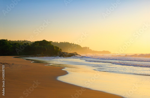 Beautiful scenic view - sea surf, wet sand, rocks and wood against the background of colorful morning sky before the sunrise in Tangalla beach, Sri Lanka island, Indian Ocean, South Asia