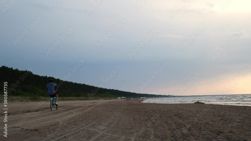Young guy goes away in the distance on a bicycle on the beach during sunset Young guy goes away in the distance on a bicycle on the beach during sunset