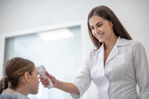 Dark-haired smiling doctor checking temperature of her small patient