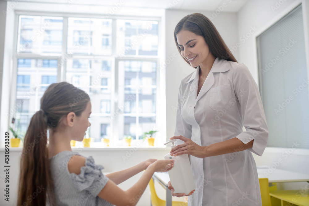 Doctor in a lab coat spraying sanitizer to girls hands Doctor in a lab coat spraying sanitizer to girls hands