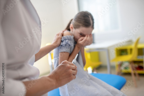 Girl looking at the syring in doctors hand and feeling scared