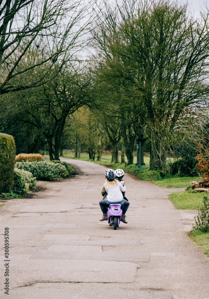 Two little girls riding along a country road on a battery-powered motorbike. Two little girls riding along a country road on a battery-powered motorbike.