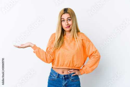 Young blonde woman isolated on white background showing a copy space on a palm and holding another hand on waist.
