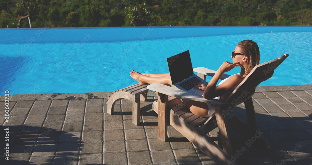 Concentrated woman working on laptop on poolside