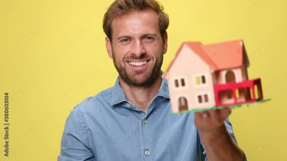 businessman laughing, holding a house model in one hand, waving his fists and celebrating succes, being excited on yellow background businessman laughing, holding a house model in one hand, waving his fists and celebrating succes, being excited on yellow background