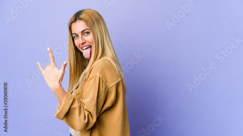 Young blonde woman isolated on purple background showing rock gesture with fingers