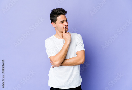 Young caucasian man isolated on purple background looking sideways with doubtful and skeptical expression.