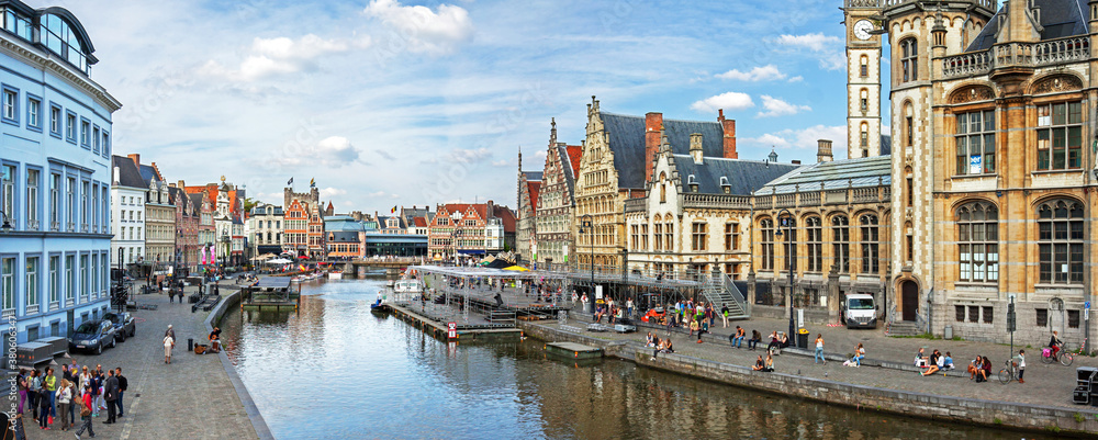 Ghent, Belgium: panoramic view on canal boats and many visitors at Graslei and Korenlei, famous for their historic facades.