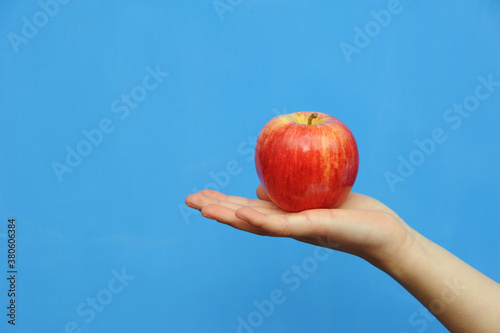 Bright red apple on a childs hand in front of a blue background