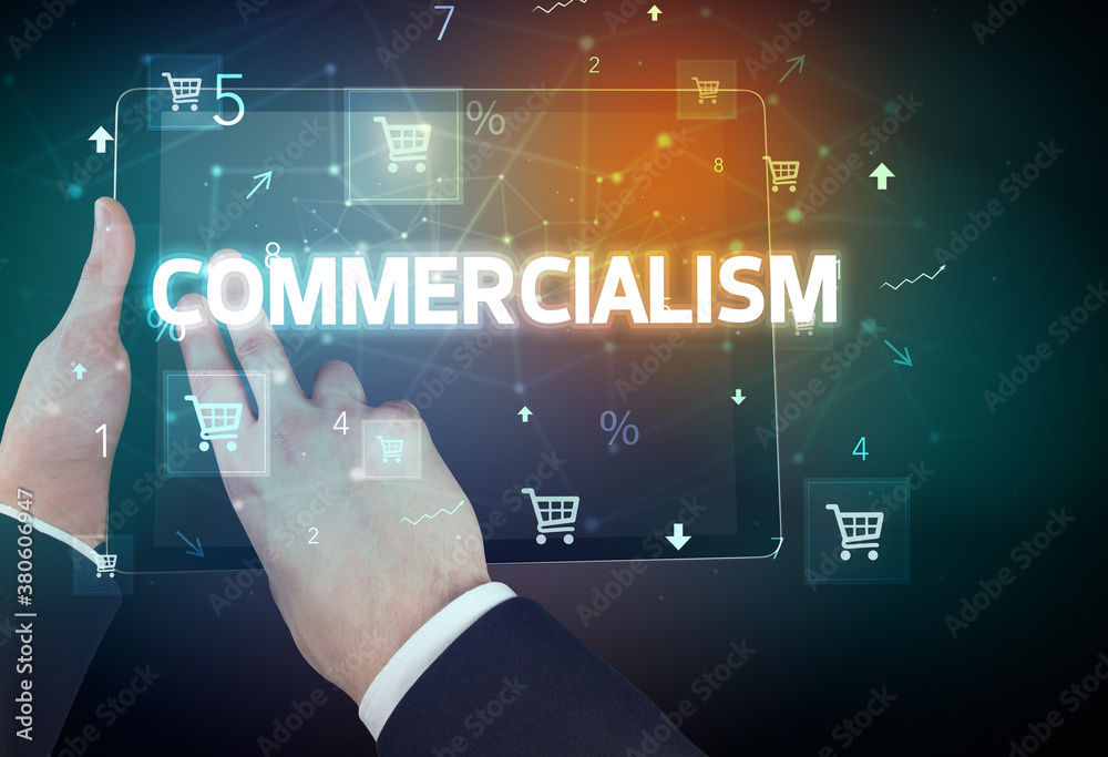 Close-up of a hand holding tablet with COMMERCIALISM inscription, online shopping concept Close-up of a hand holding tablet with COMMERCIALISM inscription, online shopping concept