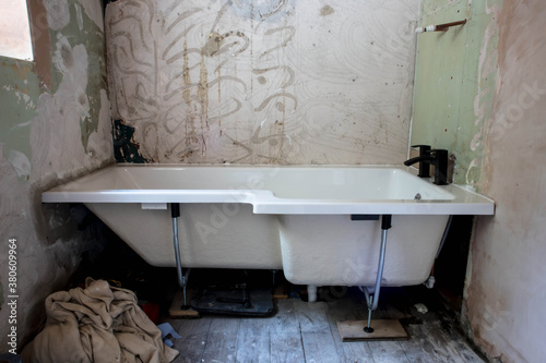 White bathtub with black taps being installed into bathroom as part of home improvements renovations.  Stripped walls