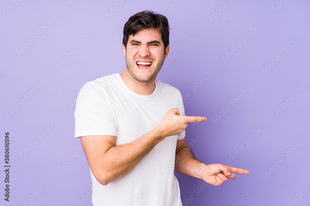 Young man isolated on purple background pointing with forefingers to a copy space, expressing excitement and desire. Young man isolated on purple background pointing with forefingers to a copy space, expressing excitement and desire.