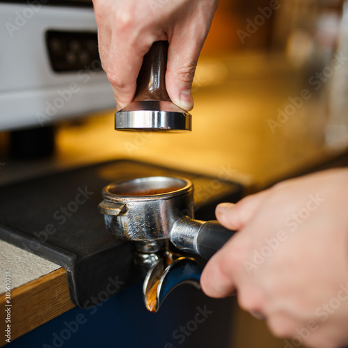 Crop male barista pressing coffee in portafilter with tamper and preparing espresso in coffee shop