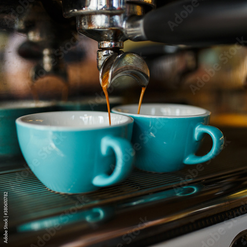 Closeup of modern coffee maker pouring aromatic hot cappuccino in blue cups in cafe for breakfast 