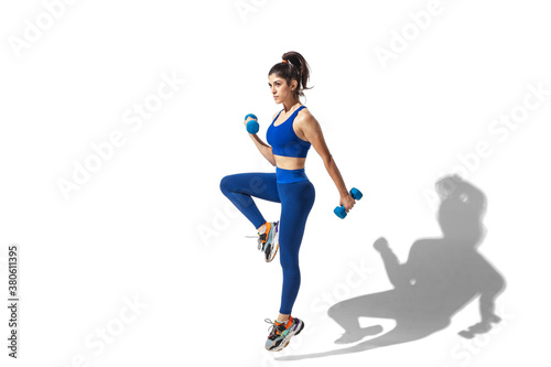 Weights. Beautiful young female athlete practicing on white studio background, portrait with shadows. Sportive fit model in motion and action. Body building, healthy lifestyle, style concept.