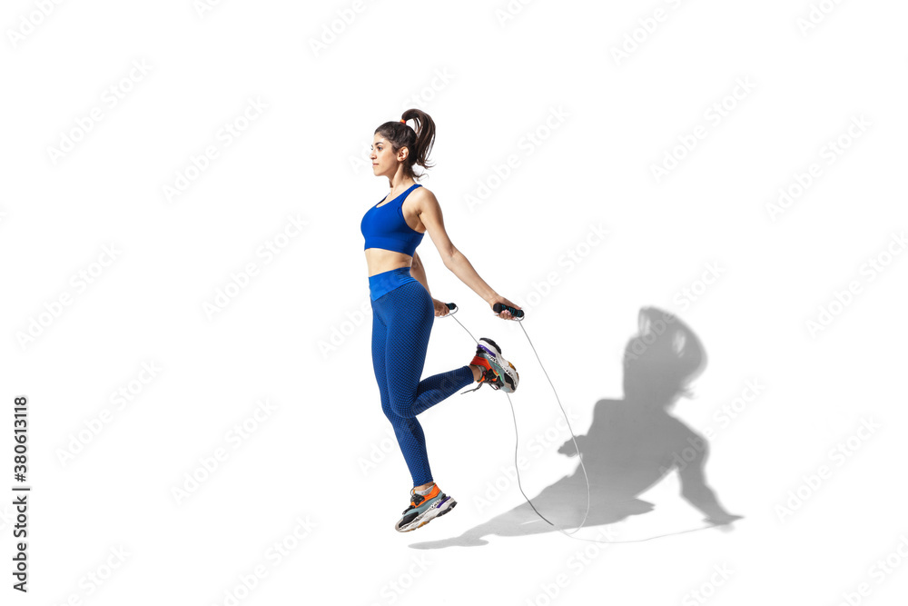 Energy. Beautiful young female athlete practicing on white studio background, portrait with shadows. Sportive fit model in motion and action. Body building, healthy lifestyle, style concept.