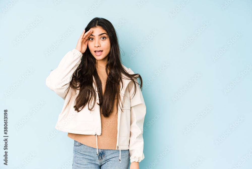 Young indian woman on blue background shouts loud, keeps eyes opened and hands tense. Young indian woman on blue background shouts loud, keeps eyes opened and hands tense.