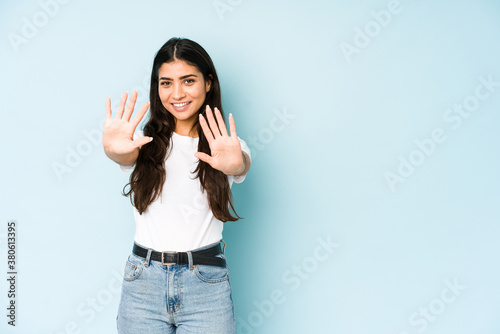Young indian woman on blue background showing number ten with hands.