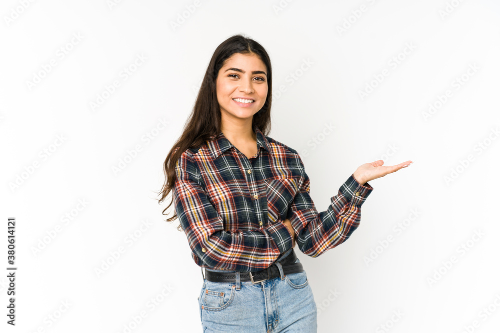 Young indian woman isolated on purple background showing a copy space on a palm and holding another hand on waist.
