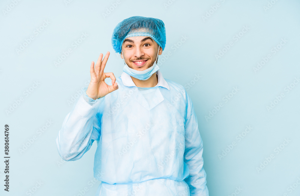 Young arabian surgeon man isolated against on a blue background cheerful and confident showing ok gesture.