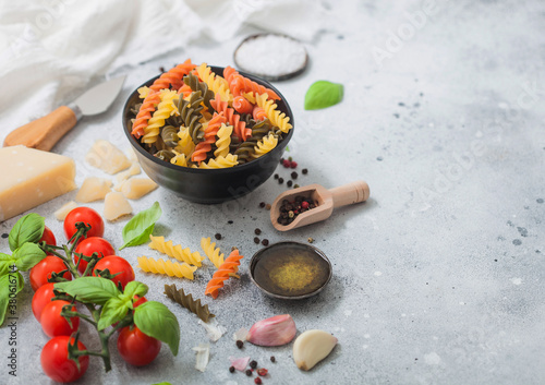 Fusilli pasta in black bowl with parmesan cheese and tomatoes, oil and garlic with basil and linen towel on light background. photo