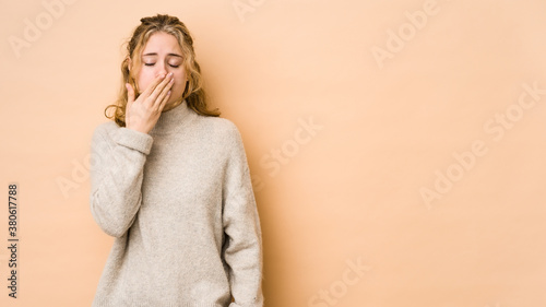 Young caucasian woman isolated on beige background yawning showing a tired gesture covering mouth with hand.