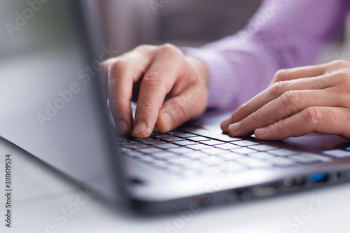 Male executive hands typing and scrolling on a laptop computer device with blur background. Working online from home. 