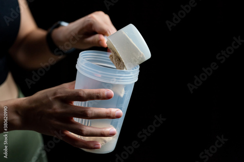 Close up of women with measuring scoop of whey protein and shaker bottle, preparing protein shake. photo