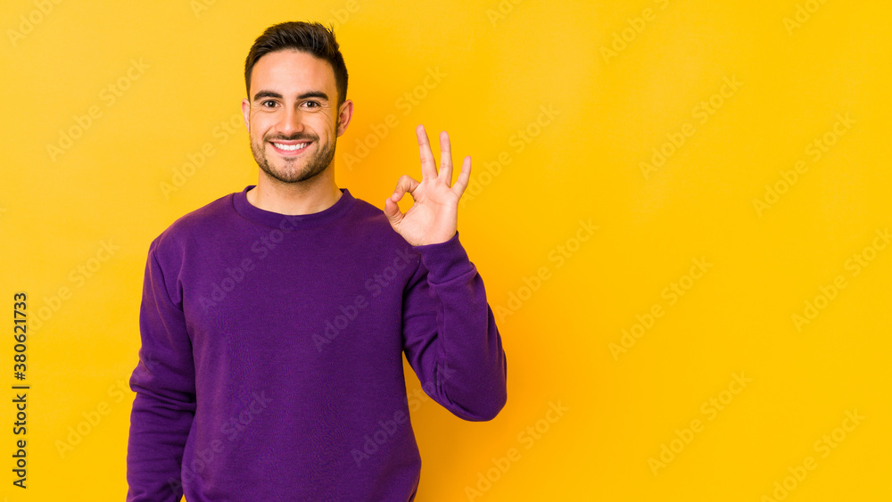 Young caucasian man isolated on yellow bakground cheerful and confident showing ok gesture. Young caucasian man isolated on yellow bakground cheerful and confident showing ok gesture.
