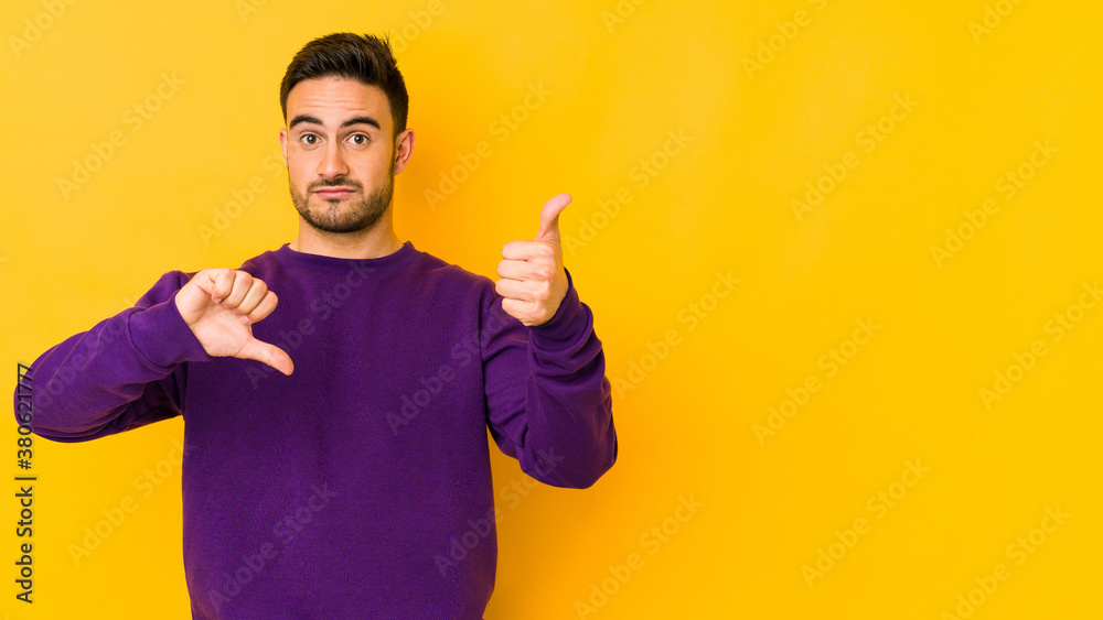 Young caucasian man isolated on yellow bakground showing thumbs up and thumbs down, difficult choose concept Young caucasian man isolated on yellow bakground showing thumbs up and thumbs down, difficult choose concept