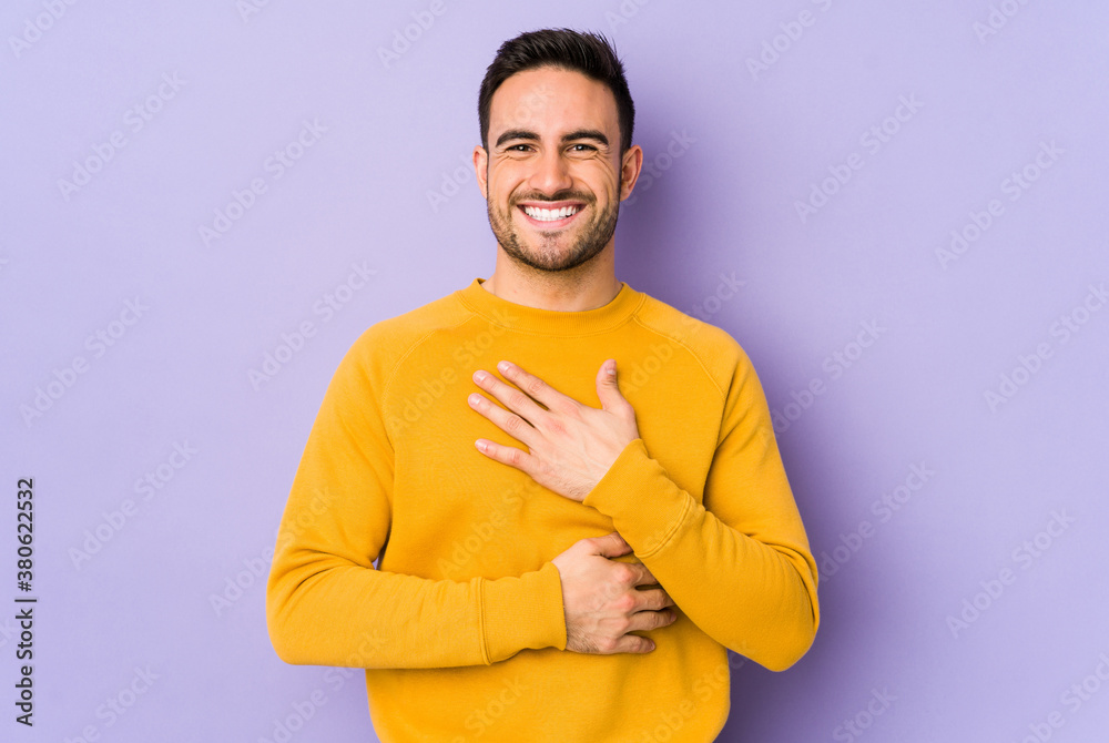 Young caucasian man isolated on purple background laughs happily and has fun keeping hands on stomach. Young caucasian man isolated on purple background laughs happily and has fun keeping hands on stomach.
