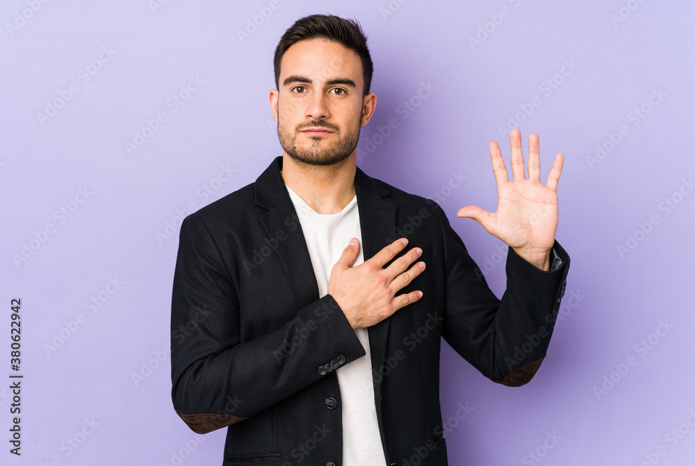 Young caucasian man isolated on purple background taking an oath, putting hand on chest.
