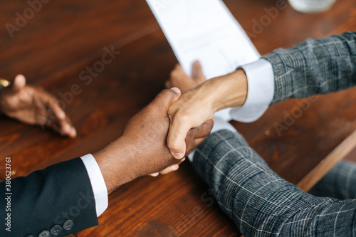 Close-up view of black and white man hands with business clothing in modern handshake to show each other friendship and respect. Concept of teamwork young business people.