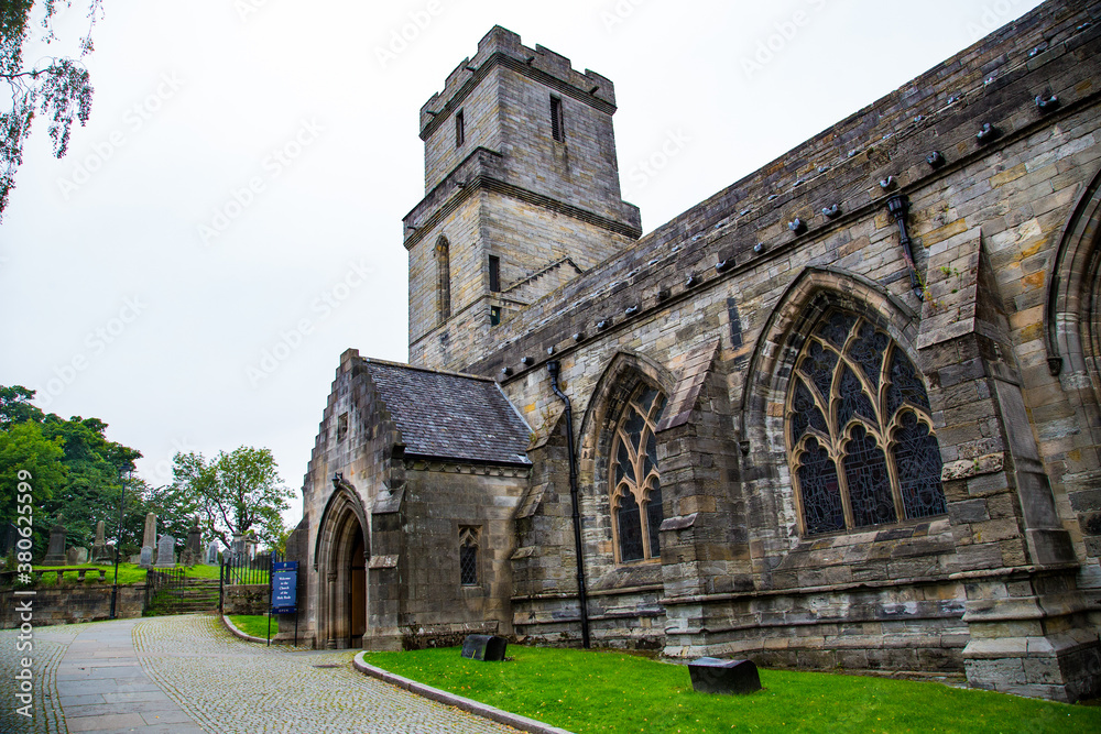 Fachada lateral de entrada de iglesia gótica con césped y adoquines