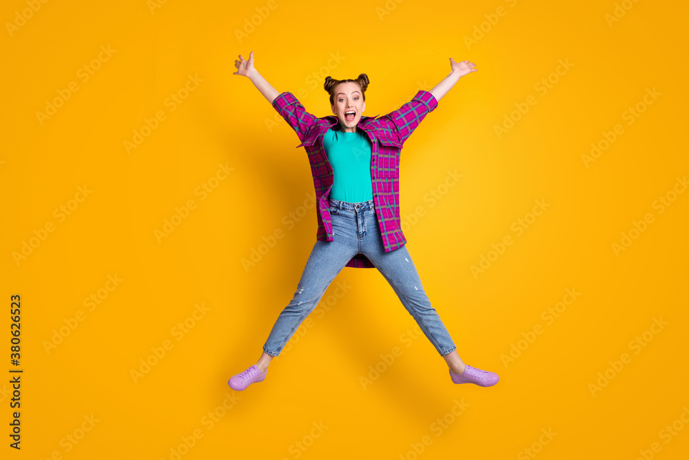 Full length photo of pretty charming crazy teen lady jump up excited good mood rejoicing star figure spread arms legs wear casual plaid shirt sneakers jeans isolated yellow color background