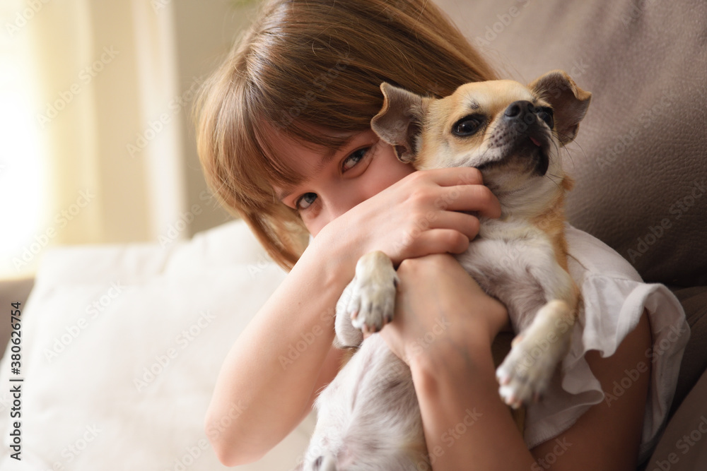 Girl stroking her dog in her arms on the sofa Girl stroking her dog in her arms on the sofa