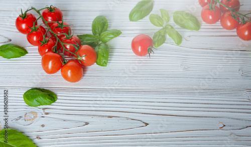 Fresh cherry tomatoes on white wooden background. Tomato red vegetable concept, copy space for text with basil leaves.