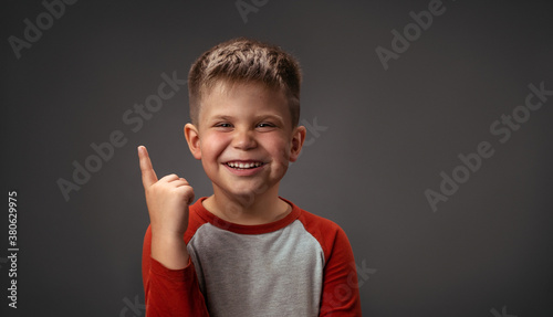 Charming boy points his finger up against an isolated background. Portrait of a smiling boy in the studio. High quality photo. photo