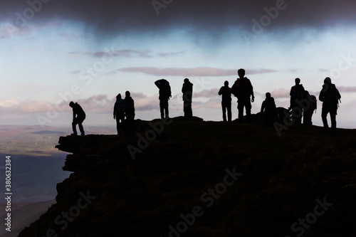 Black silhouettes of hikers on the top of a mountain resting below a grey cloud after a mountaineering ascend.