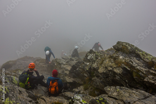 Group of mountaineers wearing helmets take a rest in the mist on rocks on the top of the mountain after scrambling in the Lake District in England.