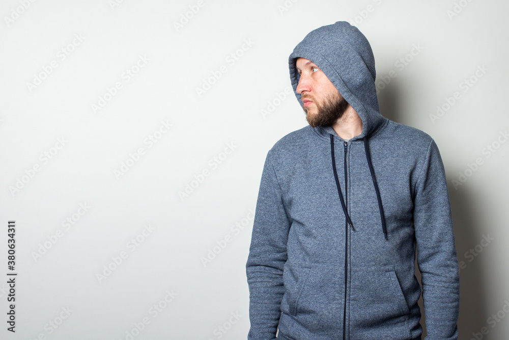 Young man in a hood with a serious, aggressive face looks to the side on a light background