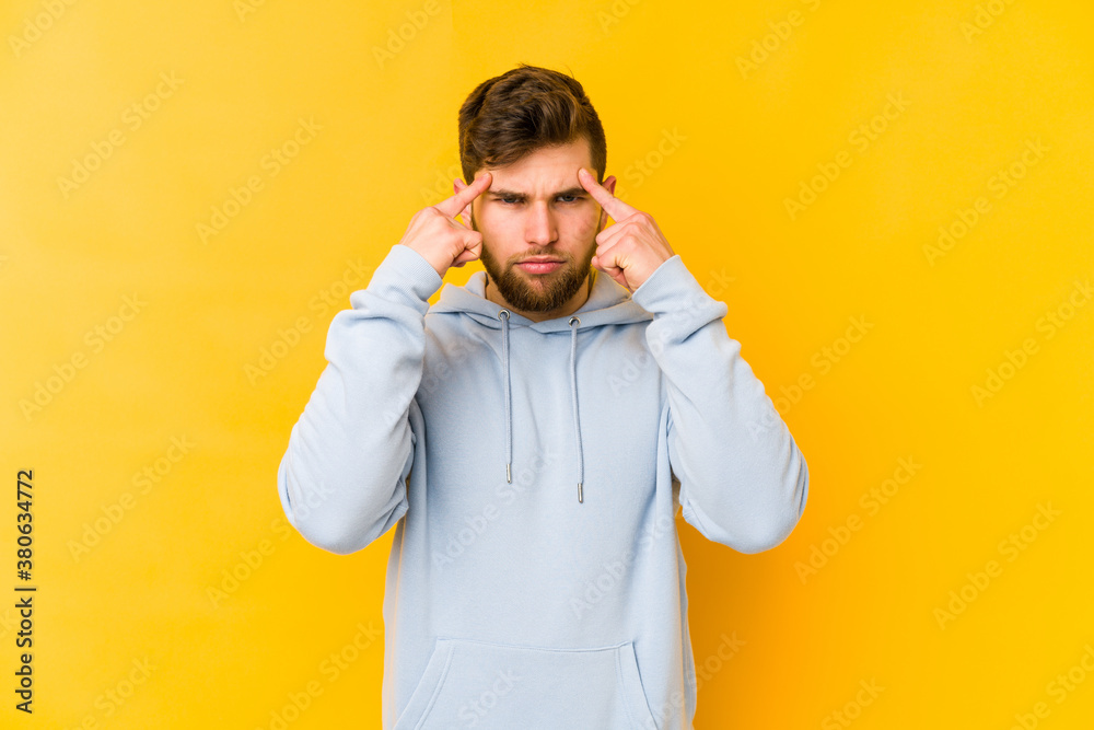 Young caucasian man isolated on yellow background focused on a task, keeping forefingers pointing head.