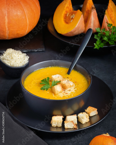 Pumpkin cream soup with cheese and croutons on black background