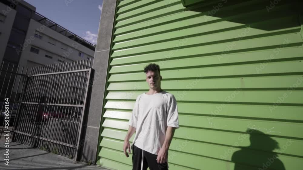 frontal shot traveling movement Caucasian boy curly black hair with short white t-shirt and long black sports pants with gray sports shoes doing parkour and flips free running in building green colors frontal shot traveling movement Caucasian boy curly black hair with short white t-shirt and long black sports pants with gray sports shoes doing parkour and flips free running in building green colors