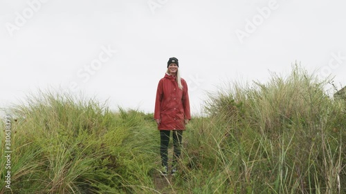 Caucasian Girl In Red Jacket Standing And Walking Away By The Grassy Path Towards The Ijmuiden Beach In The Netherlands.  - full shot photo