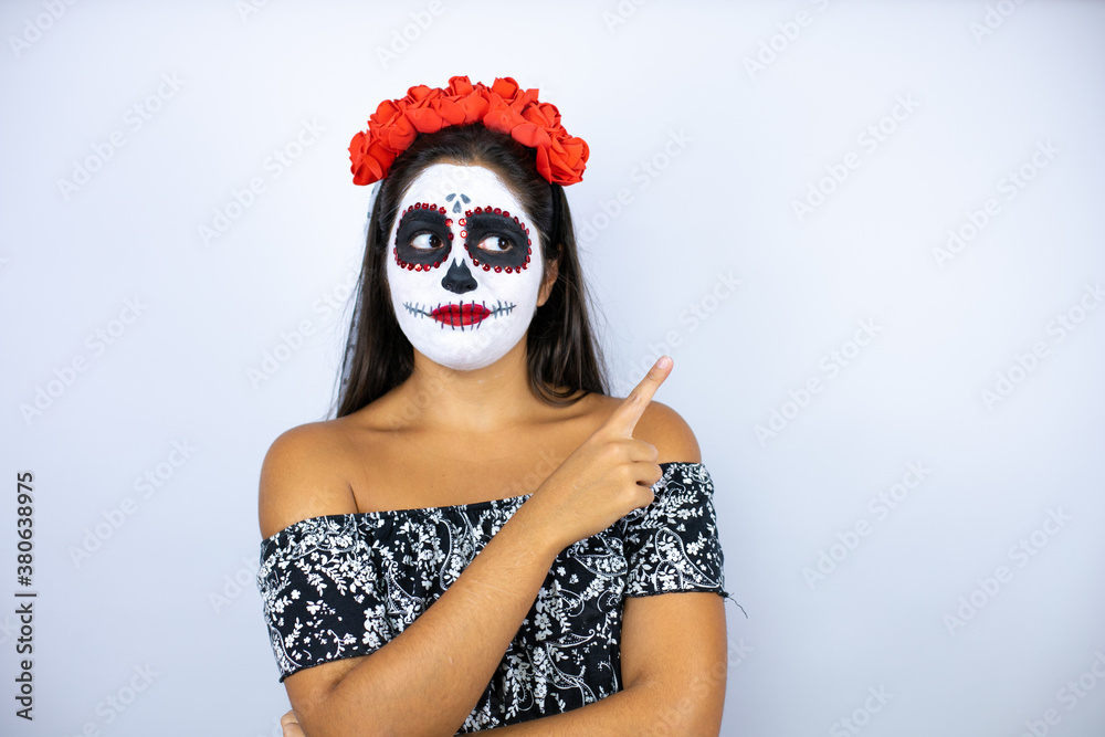 Woman wearing day of the dead costume over isolated white background smiling happy pointing with hand and finger to the side Woman wearing day of the dead costume over isolated white background smiling happy pointing with hand and finger to the side